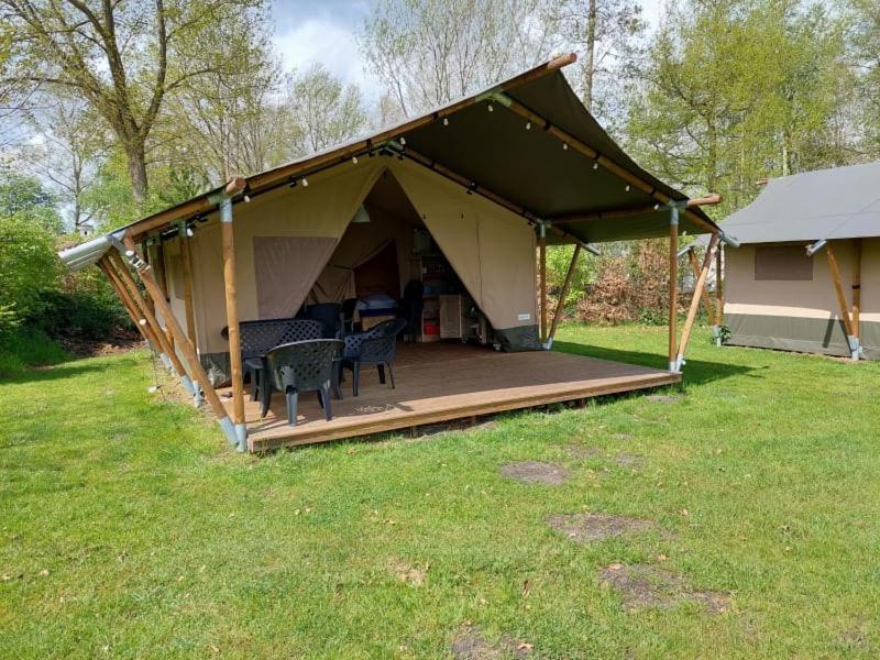 Une tente de safari avec une terrasse en bois et des chaises de jardin devant.