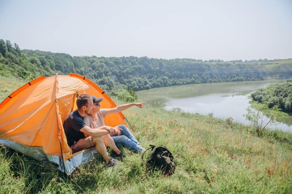 Un homme et une femme sont assis devant leur tente et admirent la vue sur la rivière.