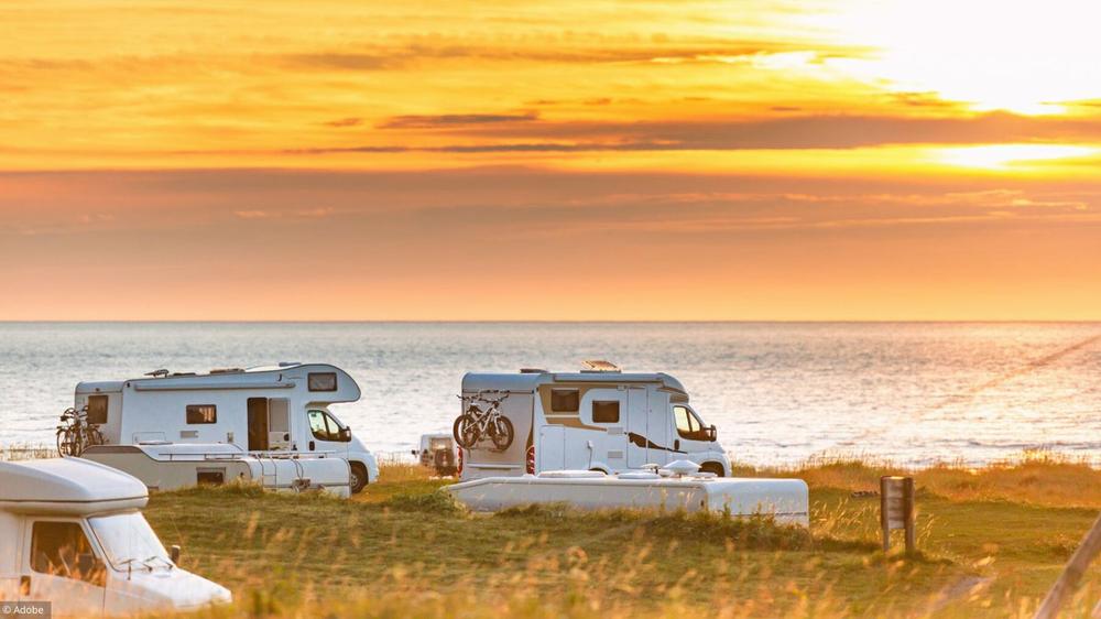 Plusieurs camping-cars stationnés sur une falaise herbeuse au bord de la mer, au soleil couchant.