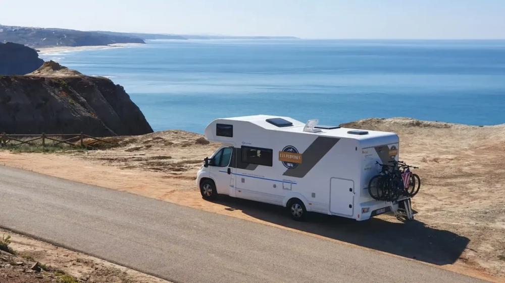 Une image dun camping-car garé sur une falaise avec la mer en arrière-plan.