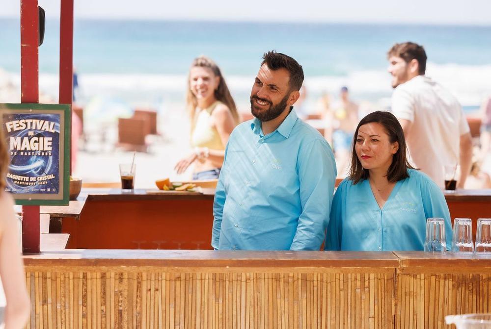 Un homme et une femme sourient en se regardant dans un bar de plage.