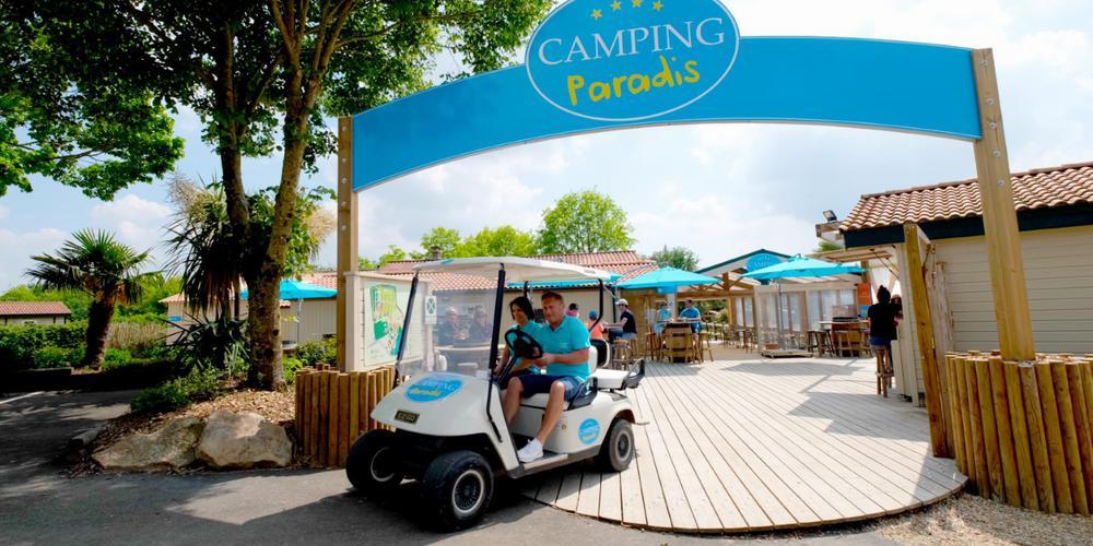 Un homme et une femme conduisent une voiturette de golf sur une allée du camping Paradis.
