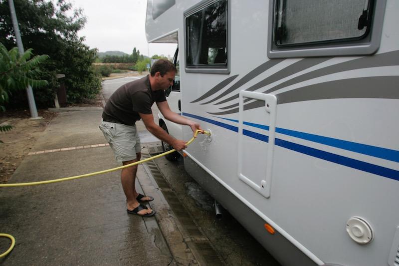 Un homme lave son camping-car avec un tuyau darrosage.