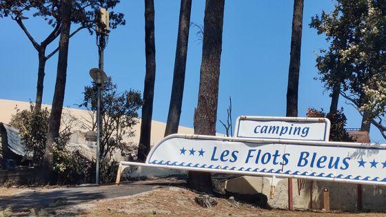 panneau indiquant camping les flots bleus devant des arbres et du sable