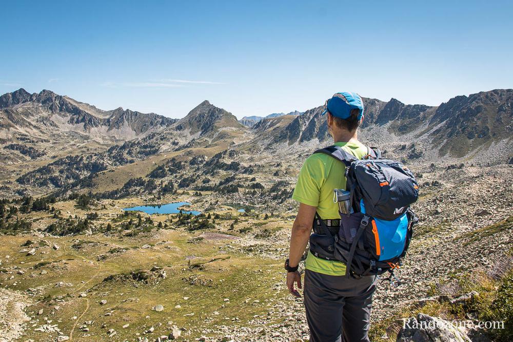 Un homme avec un sac à dos regarde un lac dans les montagnes.