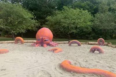Une sculpture de pieuvre rouge se trouve dans un bac à sable.