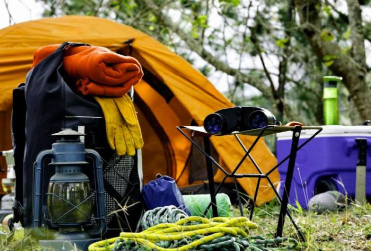 Une image montrant du matériel de camping, incluant une tente, un sac à dos, une lampe à pétrole, des jumelles et une glacière.