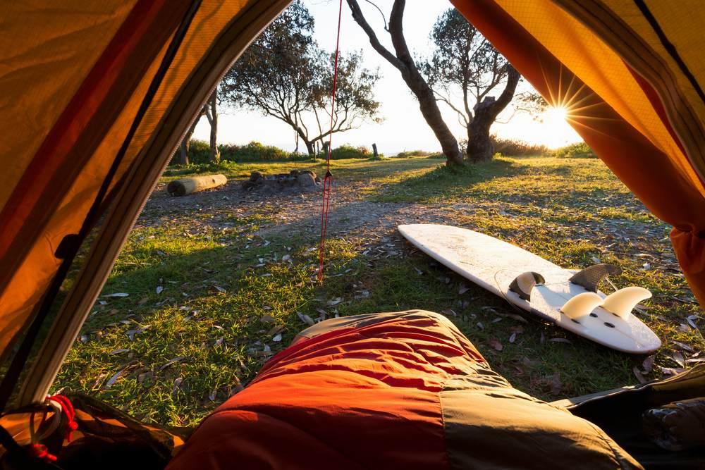 Une vue depuis lintérieur dune tente de camping, avec une planche de surf et le soleil qui se lève.