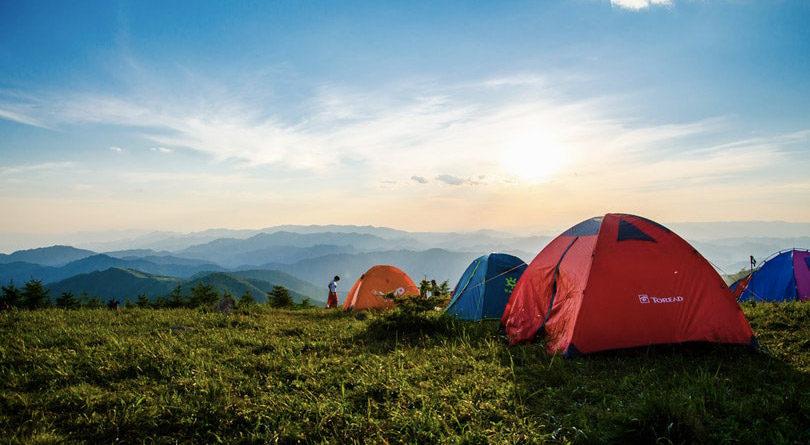 Une rangée de tentes de camping colorées sur une colline verdoyante au coucher du soleil.