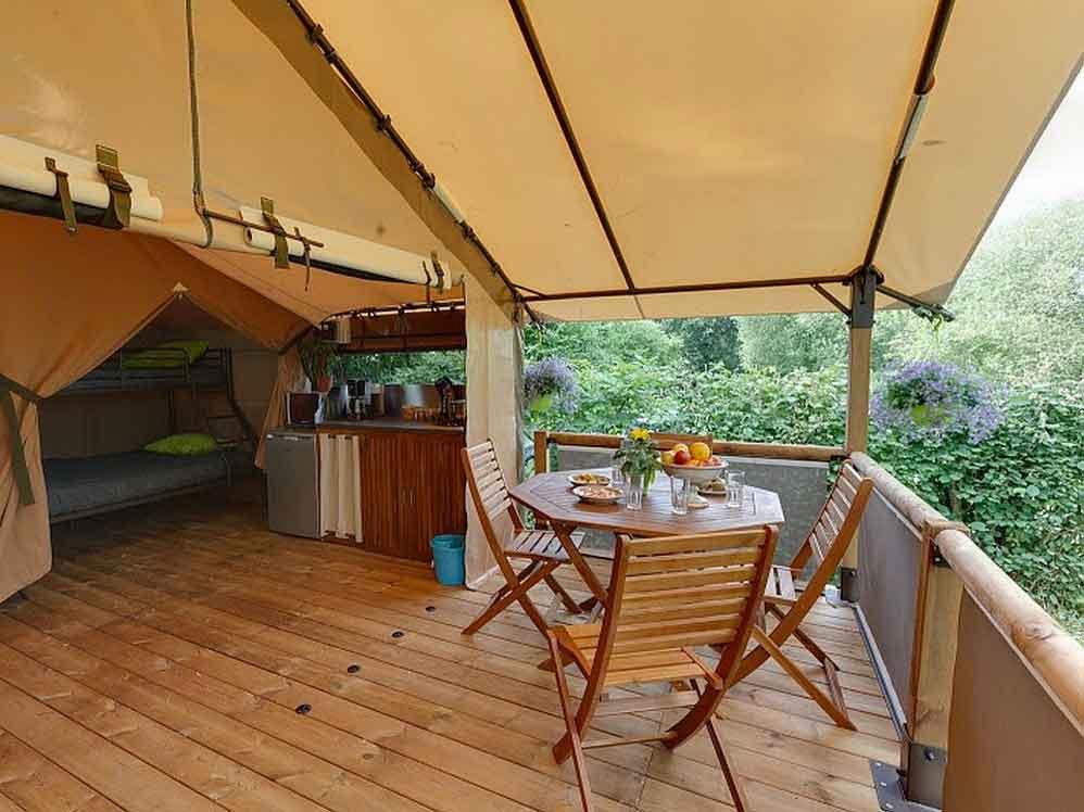 Une tente safari avec une terrasse, une table et des chaises, et une vue sur la forêt.
