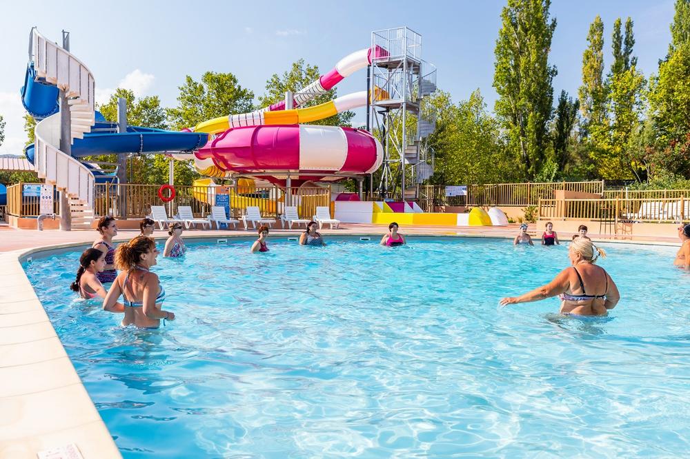 Plusieurs personnes font de laquagym dans une piscine avec un toboggan en arrière-plan.