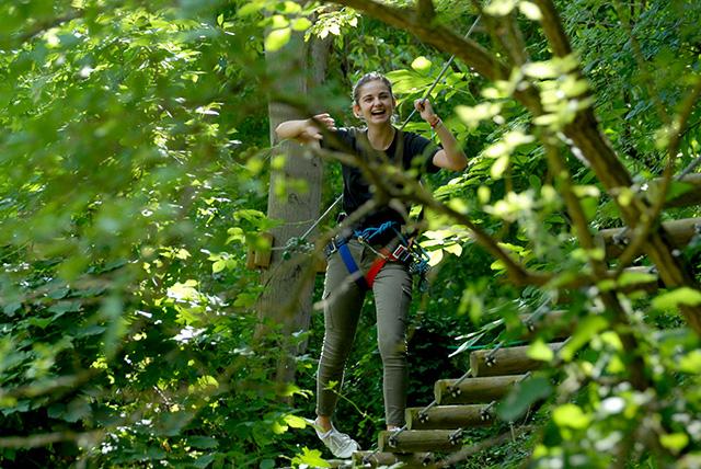 Une jeune fille souriante traverse un pont suspendu dans les arbres.
