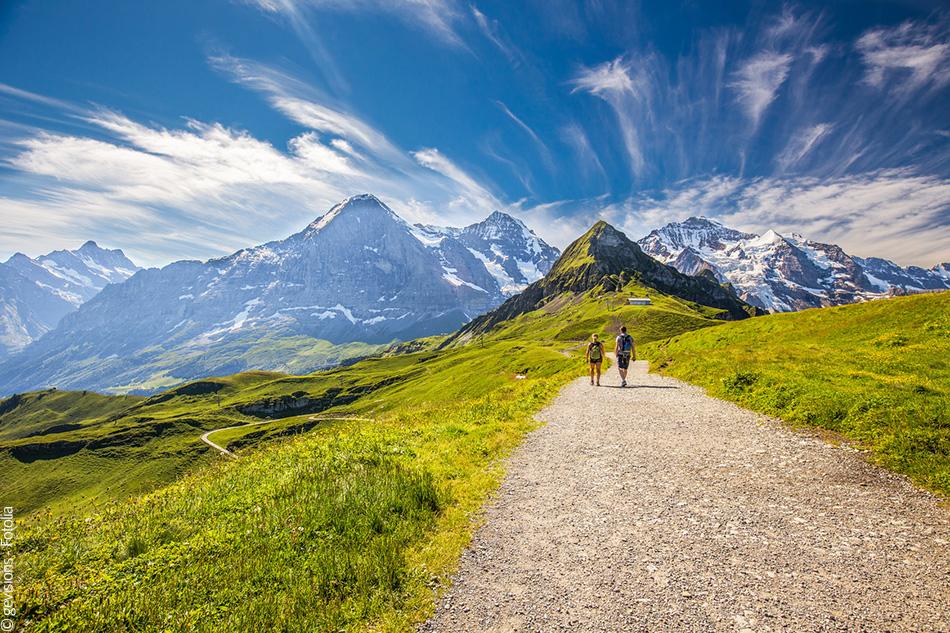 Une image dun couple marchant sur un sentier de montagne avec une vue sur les Alpes suisses.