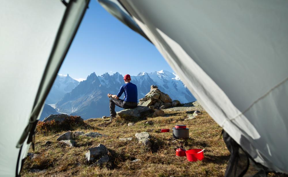 Un homme est assis sur un rocher devant une tente et regarde le Mont Blanc.