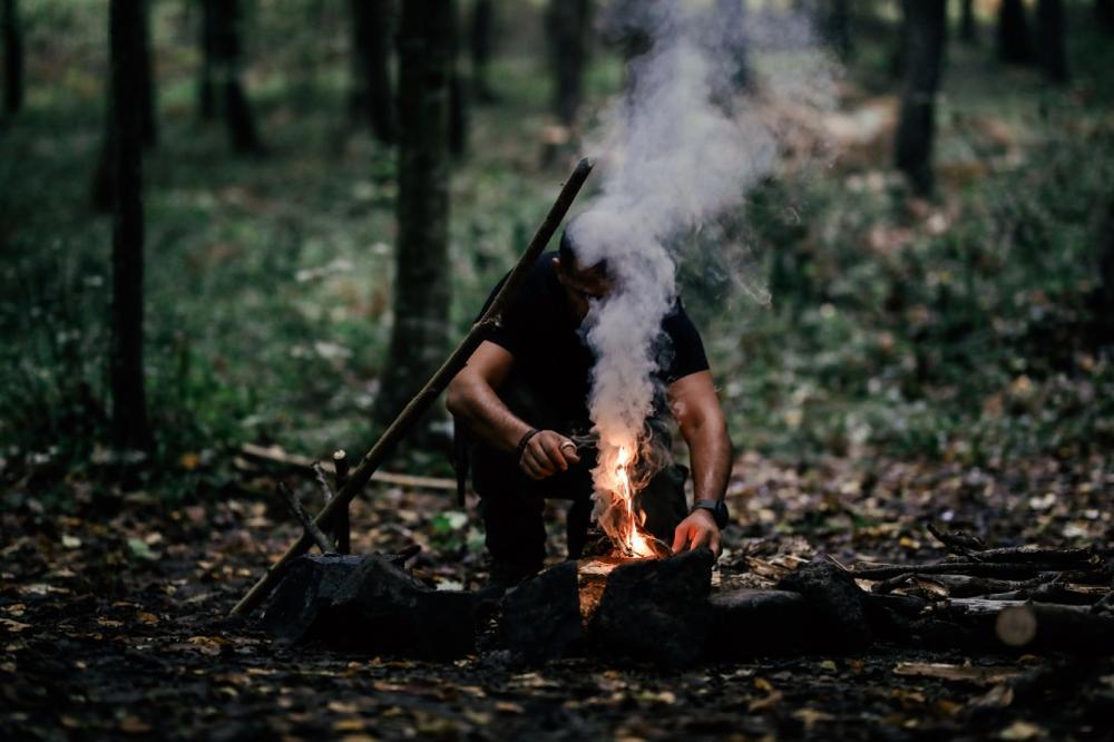 Un homme agenouillé allume un feu de camp dans les bois.