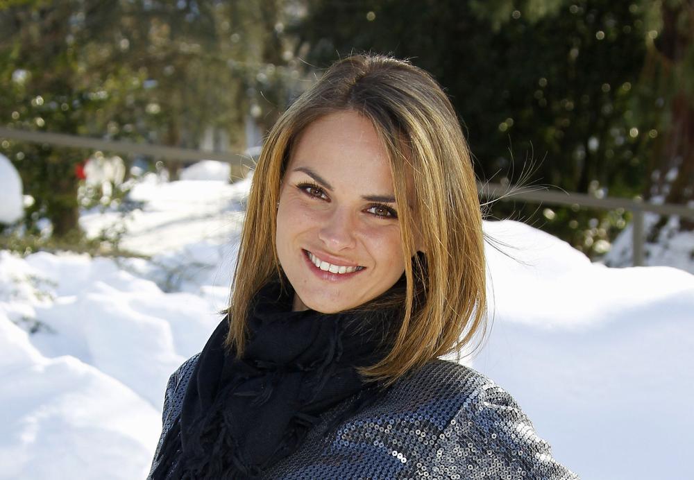 Une jeune femme blonde sourit devant un arrière-plan de neige.