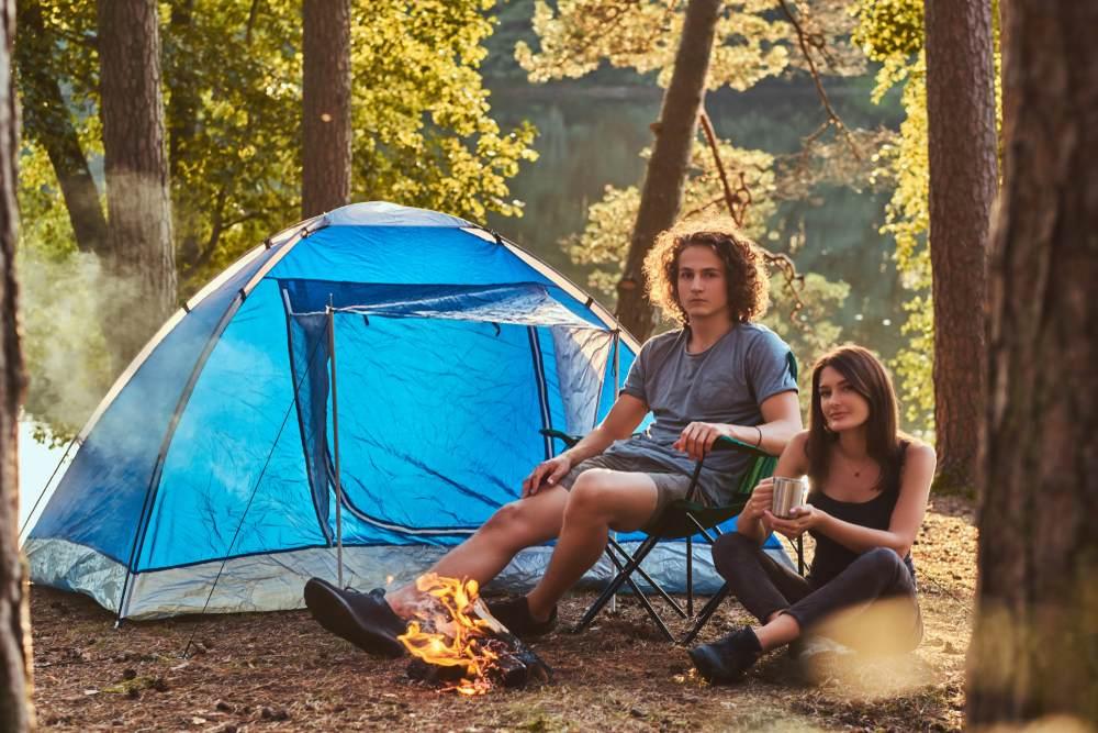 Un jeune homme et une jeune femme sont assis devant une tente bleue dans les bois.