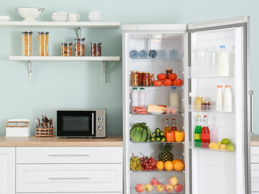 Une image dun réfrigérateur ouvert rempli de nourriture, avec un micro-ondes sur le comptoir à côté.