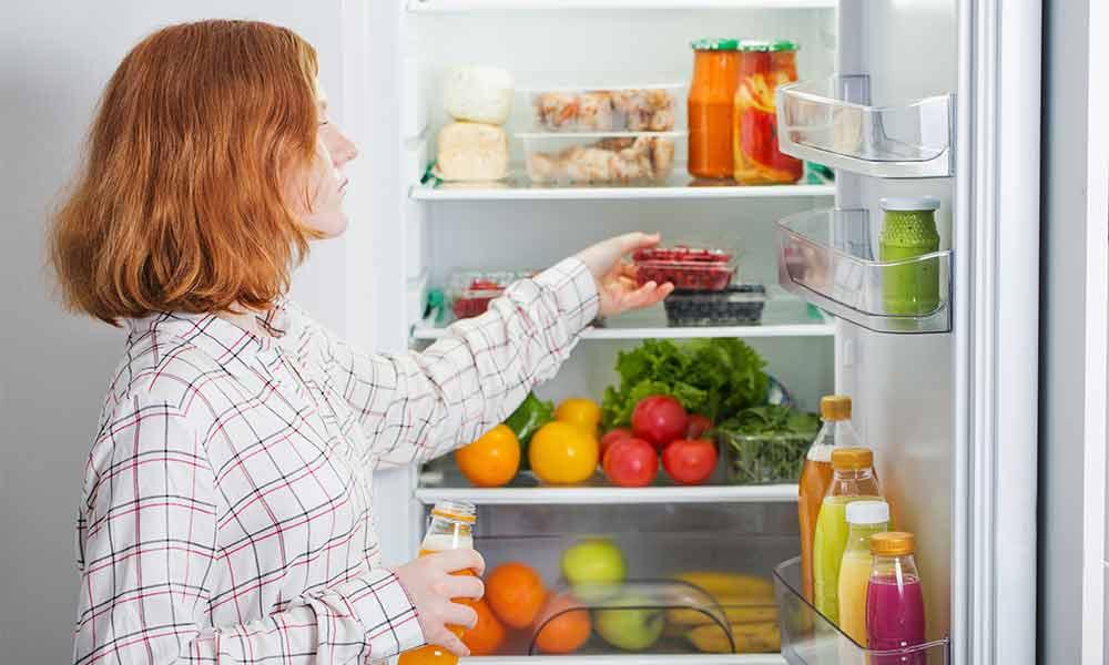 Une femme rousse se tient devant un réfrigérateur ouvert et prend un contenant de framboises.