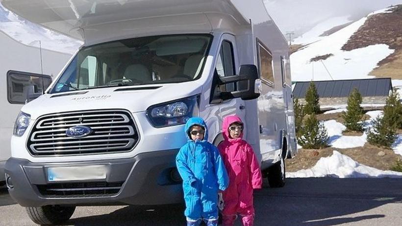 Deux jeunes enfants, habillés pour la neige, se tiennent devant un camping-car.