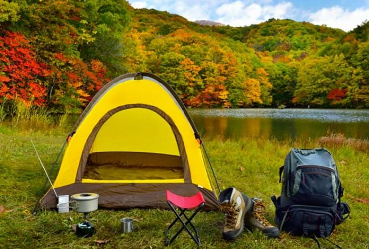 Une tente jaune est installée au bord dun lac dans une forêt colorée par lautomne.