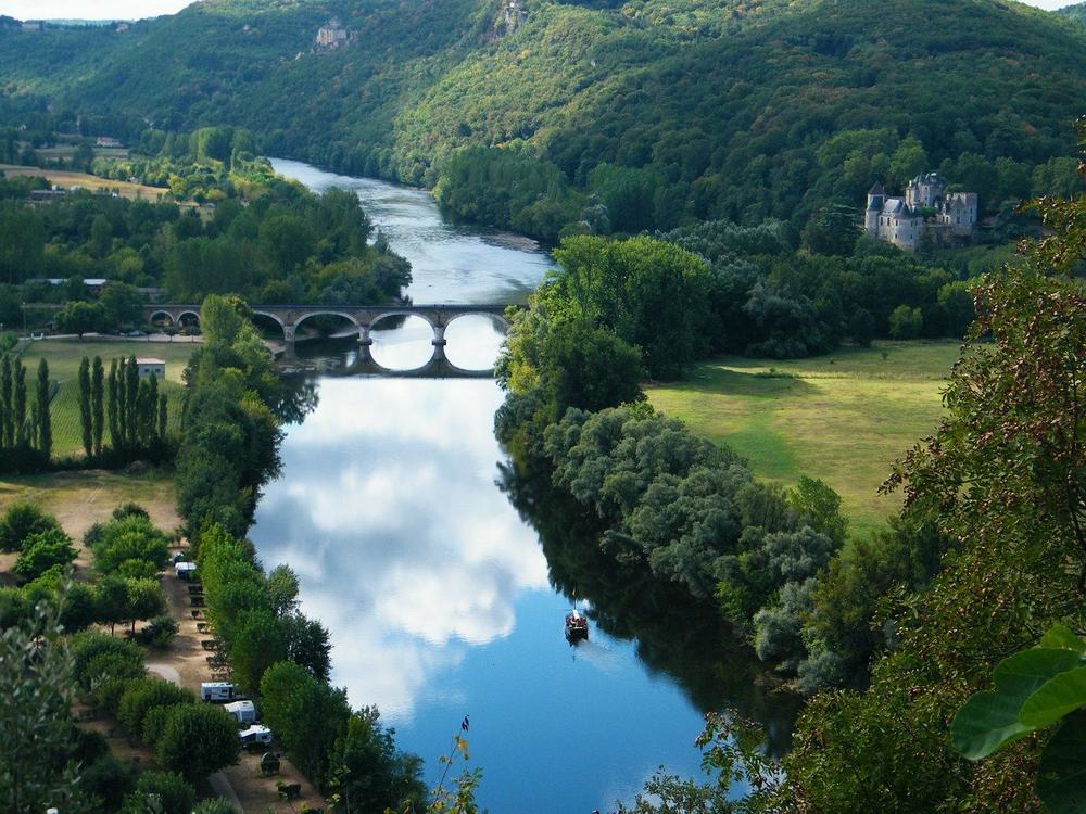 Une vue aérienne de la Dordogne, avec un pont, des arbres et un château.