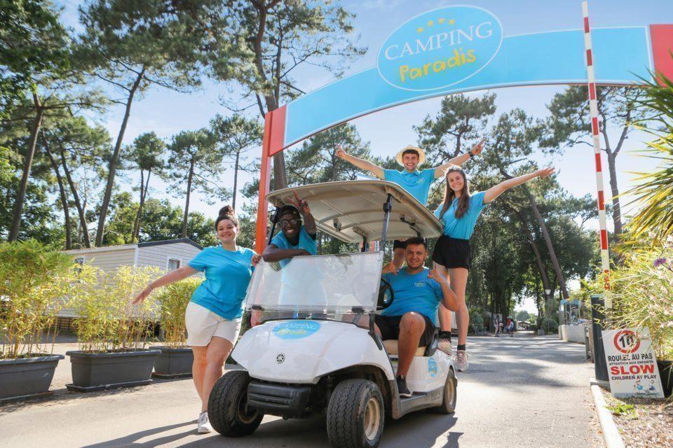 Une image de cinq personnes souriantes, dont quatre sont debout et une est assise dans une voiturette de golf.