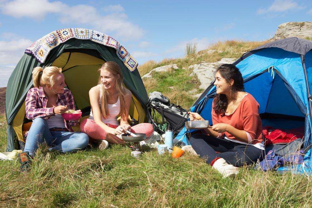 Trois jeunes femmes sont assises devant leur tente et en train de manger.