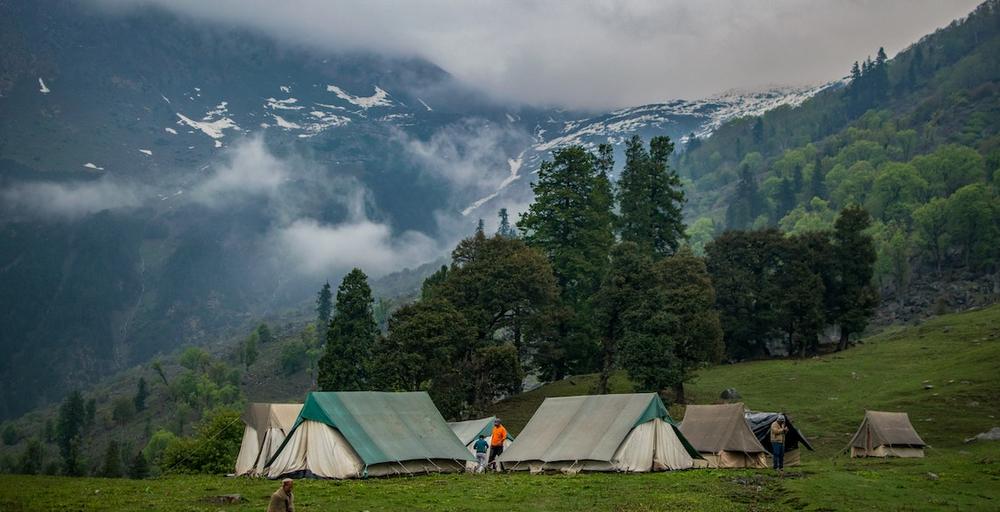 Une image de plusieurs tentes de camping dans un pré avec des montagnes en arrière-plan.