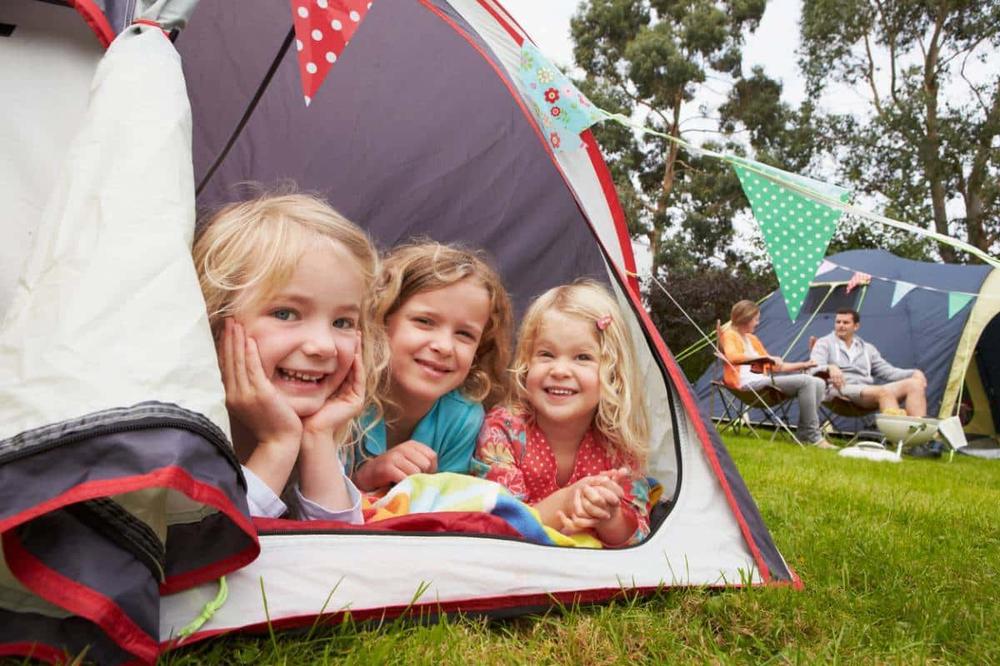 Trois jeunes filles souriantes allongées dans une tente ouverte.