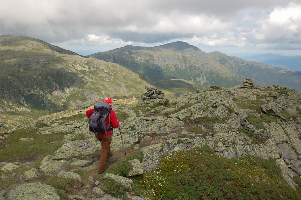 Une femme en équipement de randonnée marche sur un sentier rocheux en montagne.