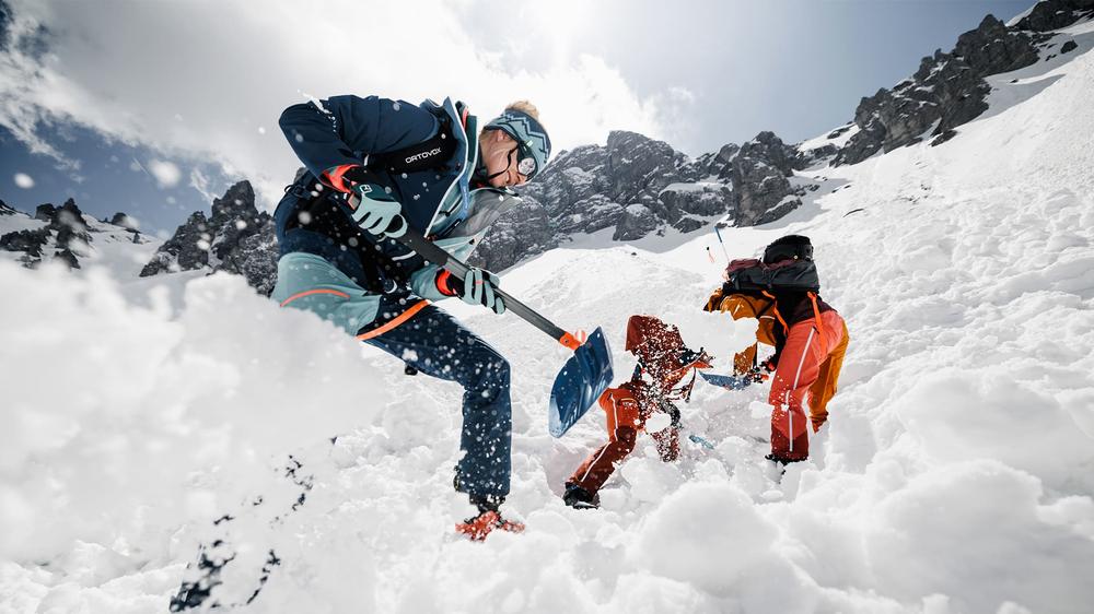 Deux skieurs en train de pelleter la neige pour dégager un troisième skieur enseveli dans une avalanche.