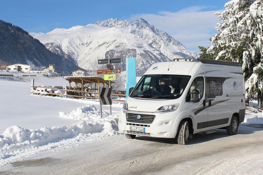 Fourgon aménagé en camping-car sur une route enneigée dans les Alpes.