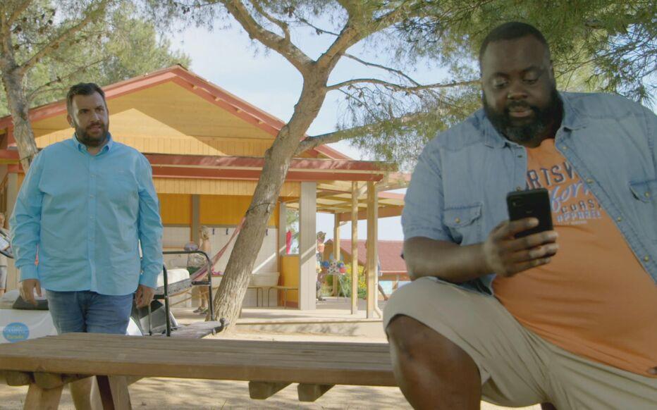 Deux hommes sont assis sur un banc, lun deux consulte son téléphone.