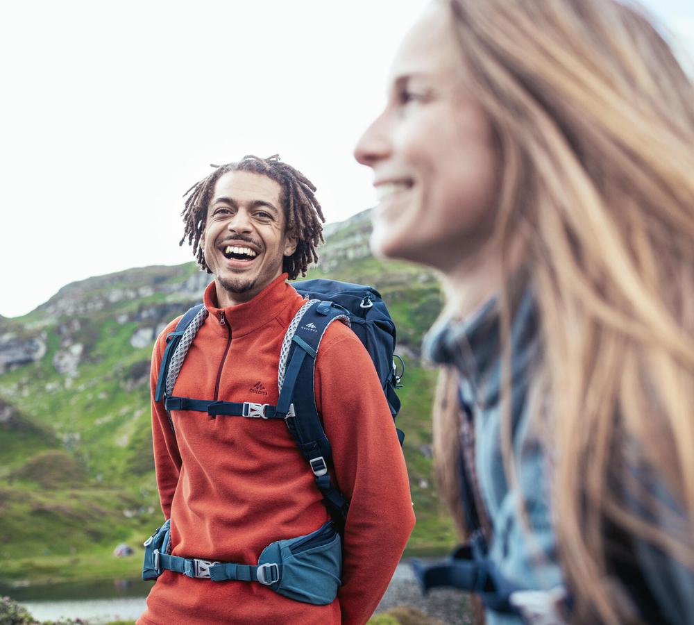 Un homme et une femme sourient en se regardant, ils sont en randonnée en montagne.