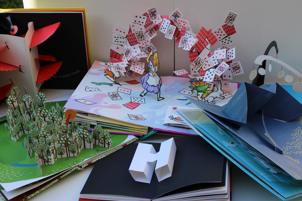 Une image montrant plusieurs livres pop-up, dont un livre Alice au pays des merveilles.