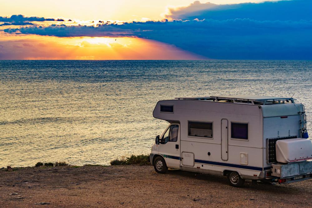 Une image dun camping-car garé sur une falaise avec la mer en arrière-plan.