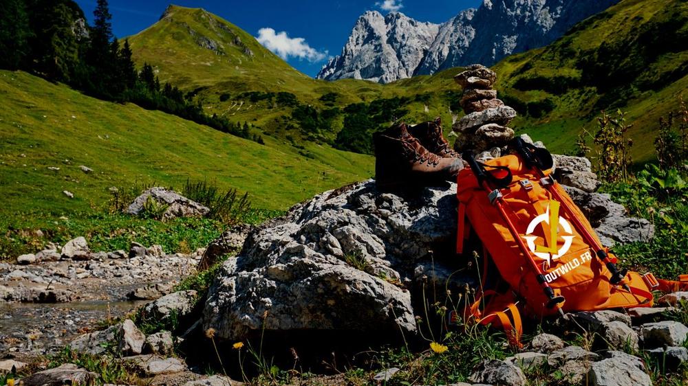 Une paire de chaussures de randonnée, un sac à dos et des bâtons de randonnée sont posés sur un rocher au bord dun ruisseau dans les montagnes.