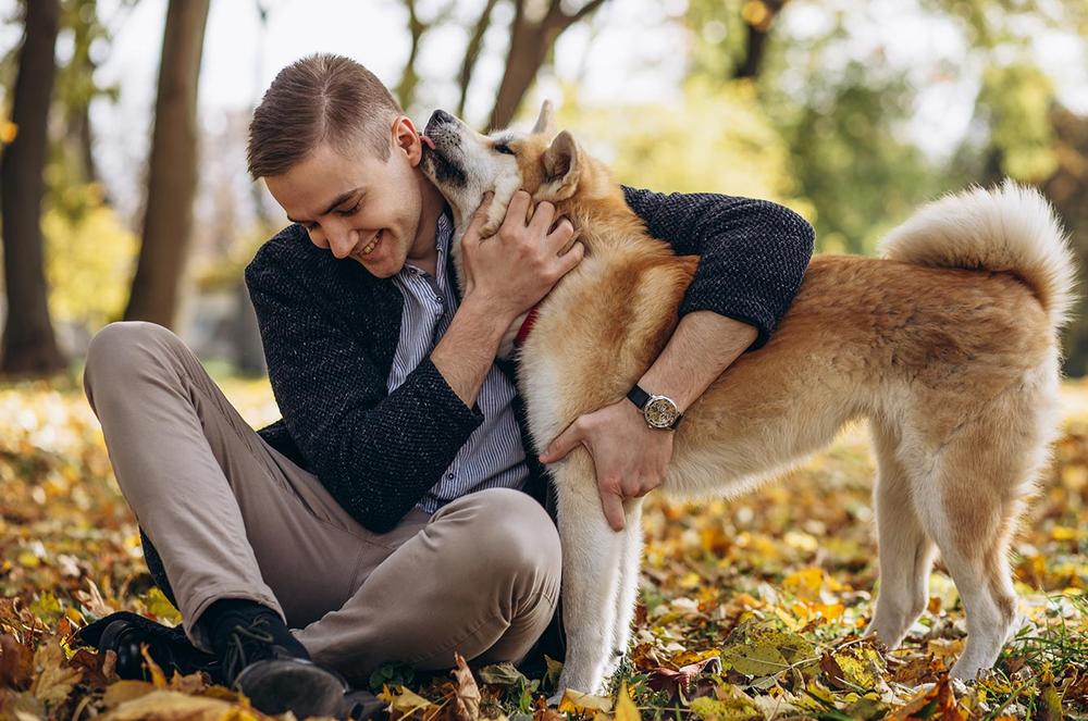 Un jeune homme est assis sur les feuilles dautomne et embrasse son chien.