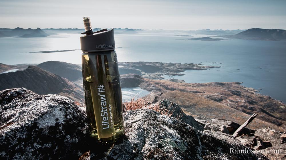Une bouteille deau LifeStraw sur un rocher avec une vue sur la mer et les montagnes en arrière-plan.