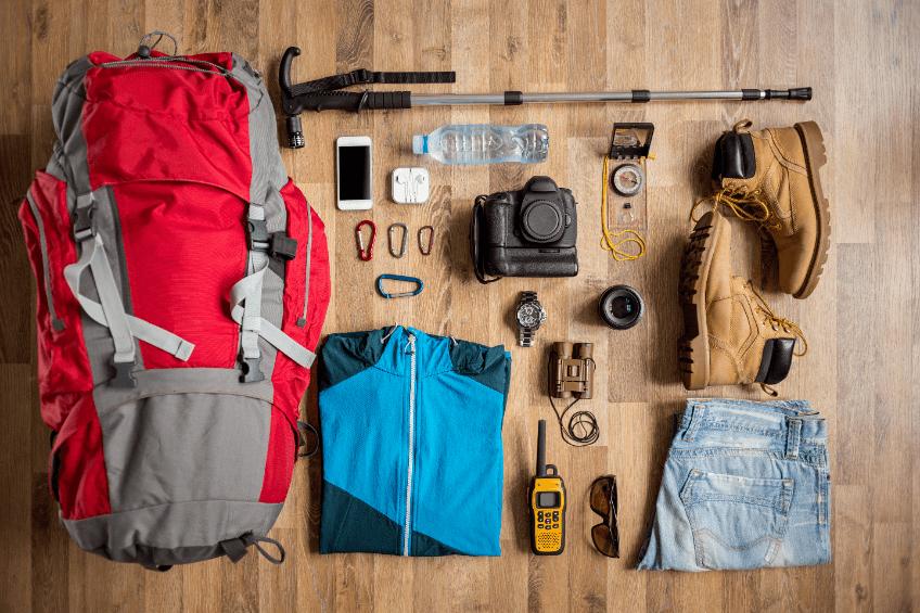 Une image montrant du matériel de randonnée, incluant un sac à dos, des chaussures, des vêtements, une gourde, une boussole et des jumelles.