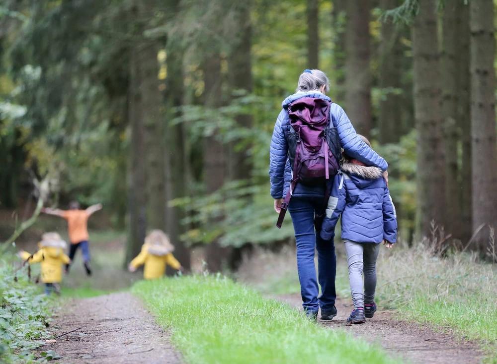 Une femme et deux enfants marchent sur un sentier forestier.