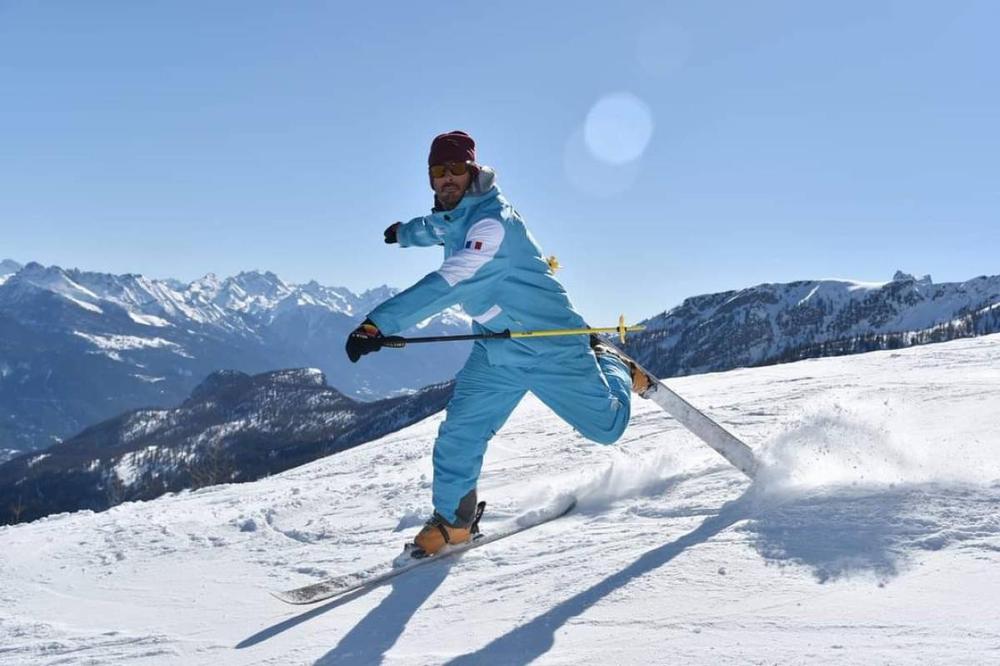 Un homme en combinaison de ski bleue descend une piste de ski.