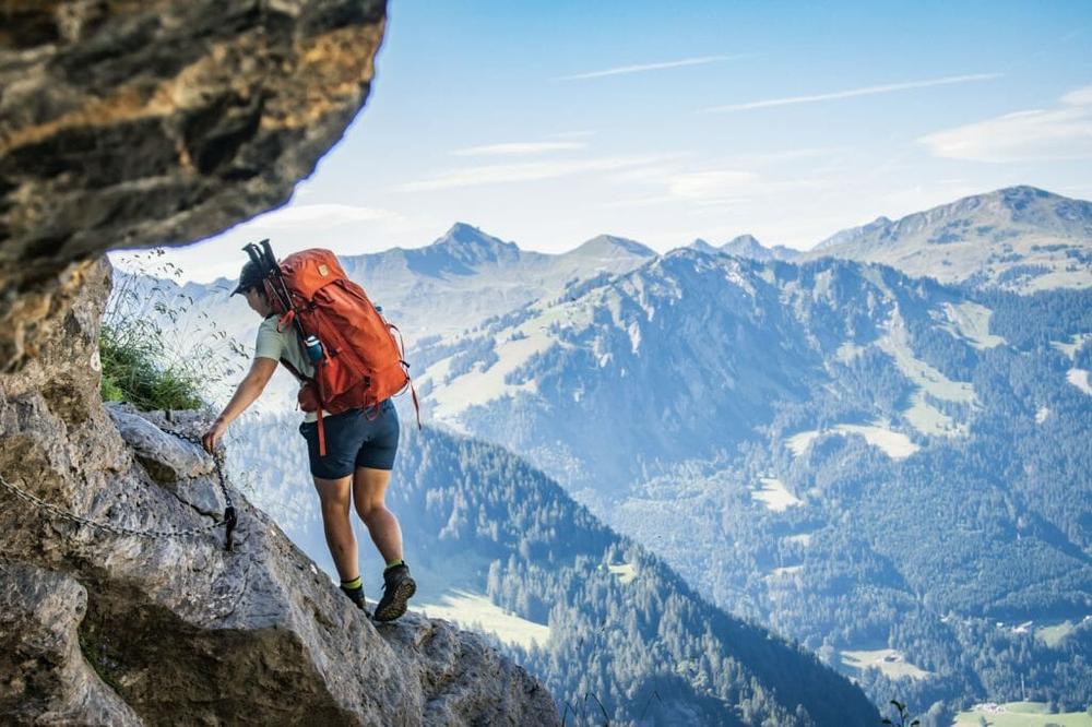 Une femme en train de grimper sur un rocher avec un sac à dos et des bâtons de randonnée.