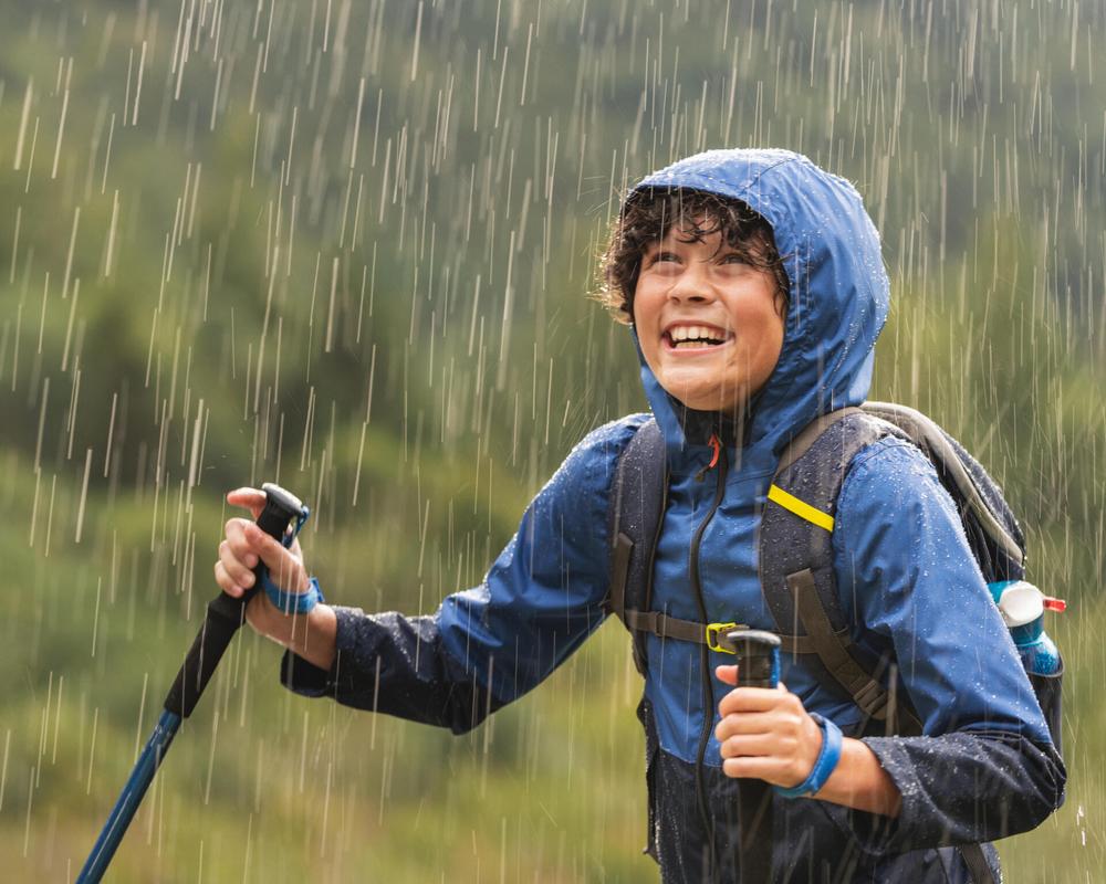 Un jeune garçon sourit et marche sous la pluie.