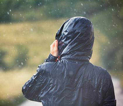 Une personne portant une veste noire avec un capuchon sur la tête se tient dans un champ sous la pluie.