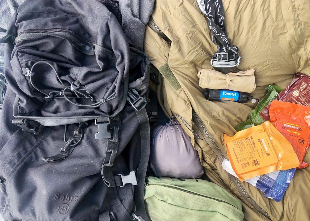 Une image montrant du matériel de camping, incluant un sac à dos, un sac de couchage, un réchaud et de la nourriture lyophilisée.