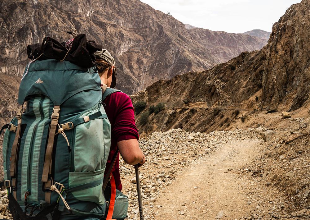 Une femme portant un sac à dos et marchant sur un sentier de randonnée en montagne.