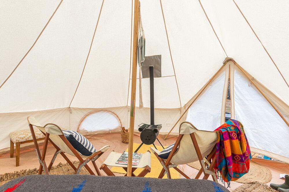 Une tente de luxe avec un poêle au centre et deux chaises Adirondack.
