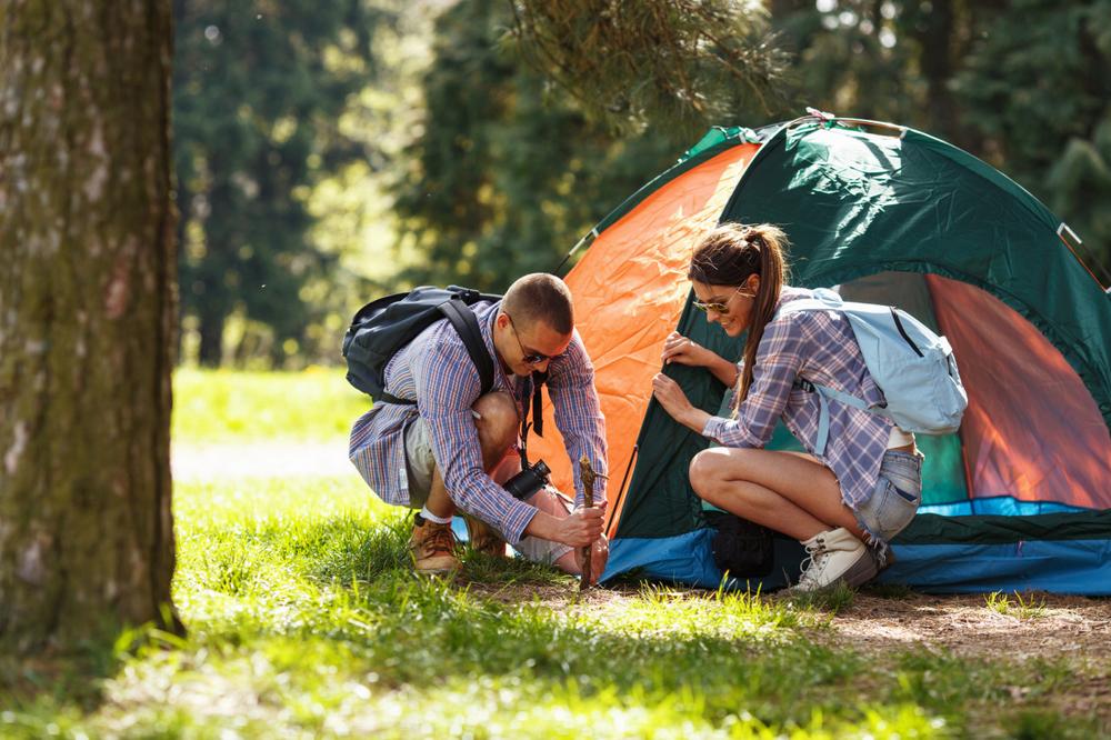 Un homme et une femme installent une tente verte et orange dans une forêt.